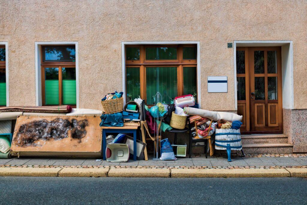 Gegenstände und Möbel stapeln sich auf dem Gehweg vor einem Haus, Teil einer Haushaltsauflösung in Düsseldorf.
