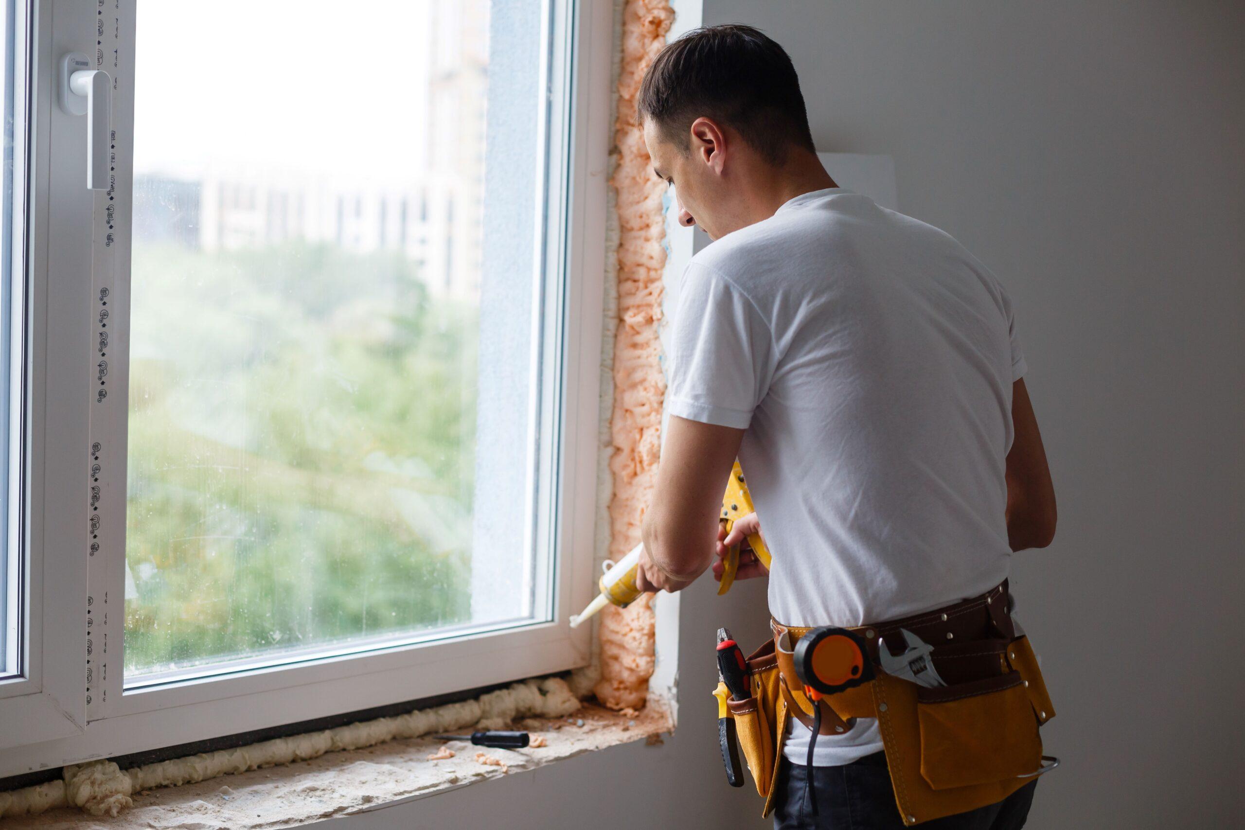 Handwerker beim Abdichten eines neu installierten Fensterrahmens in einem Wohnraum