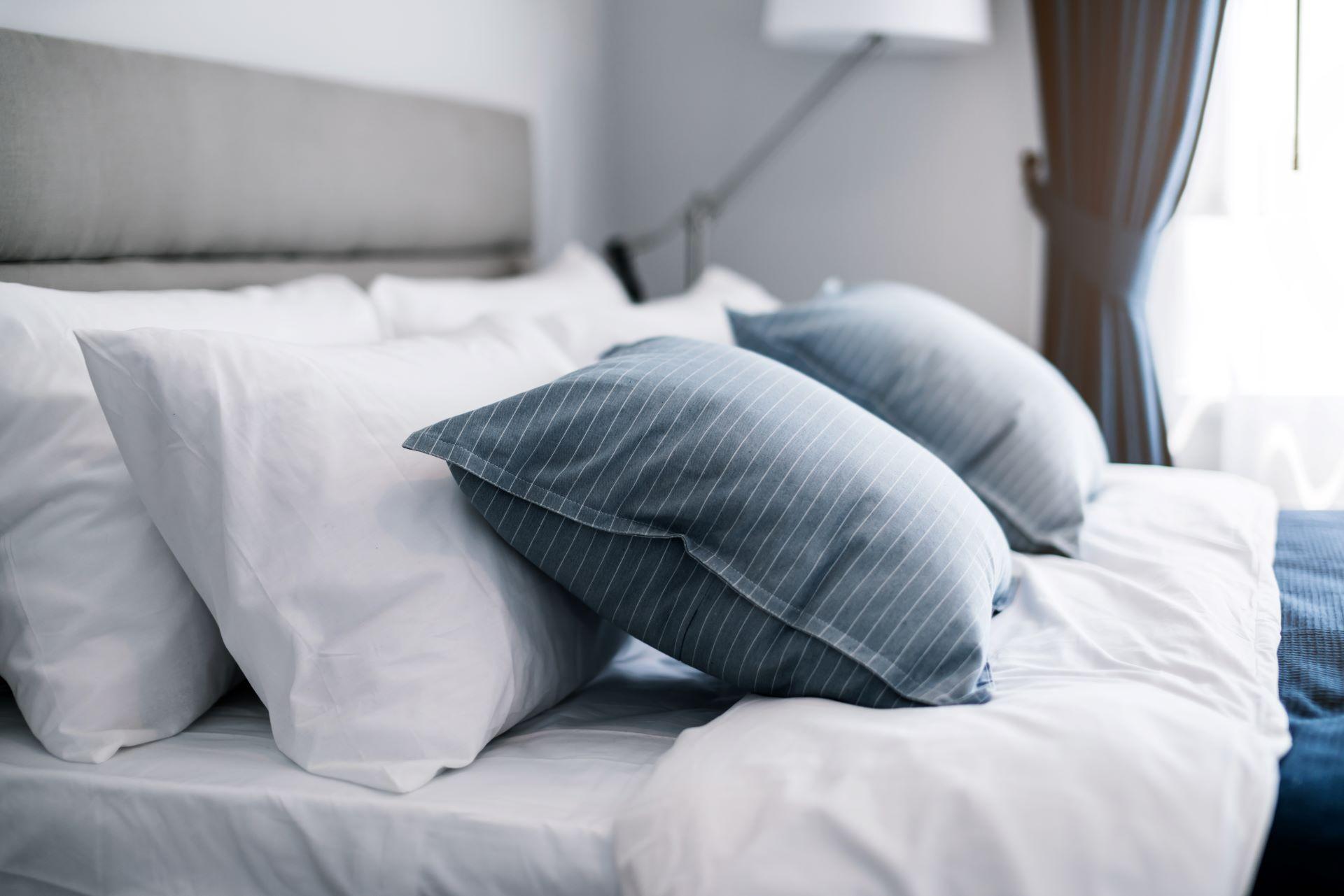 Bett mit sauberen weißen Kissen und Bettlaken im Schlafzimmer, im Sonnenlicht.