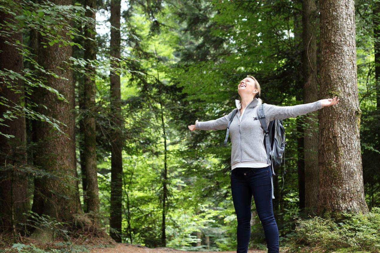 Eine Frau genießt die frische Waldluft mit ausgestreckten Armen – natürliche Wege zur Immunstärkung durch Bewegung und Propolis Tropfen.