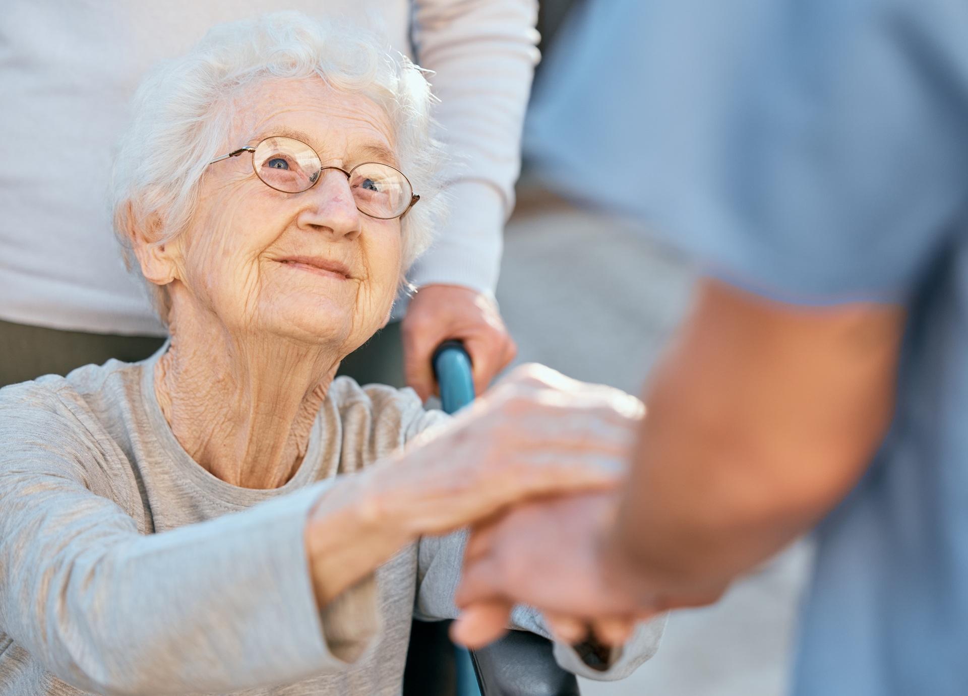 Seniorin im Rollstuhl hält Hand einer Pflegekraft | Pflegehilfskraft Frankfurt
